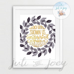 May include: A white framed print with a watercolor wreath of gray leaves. The text in gold lettering reads "God has shown us undeserved grace. By choosing to save all people. Titus 2:11".