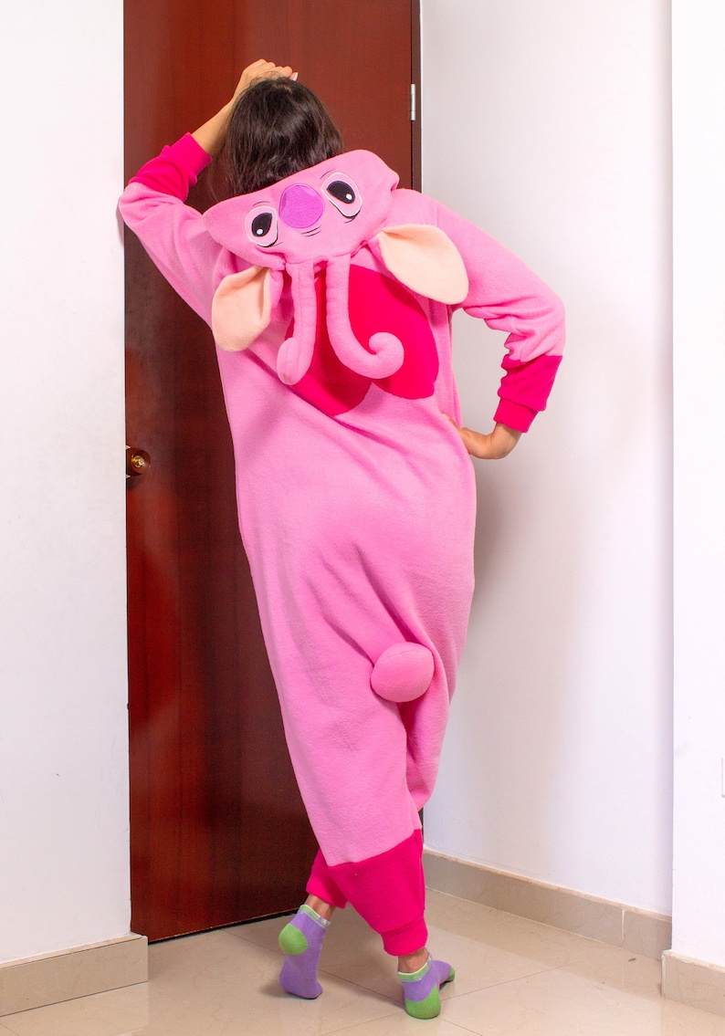 Puede incluir: Pijamas de una pieza rosa para adulto con una gran cabeza de elefante rosa en la capucha. El pijama tiene una cola rosa y detalles rosas en los pu&ntilde;os y los tobillos.