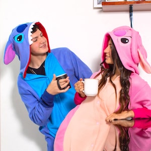 Puede incluir: Dos personas con pijamas de animales con capucha azul y rosa est&aacute;n sosteniendo tazas. La persona con el pijama azul est&aacute; mirando a la persona con el pijama rosa.