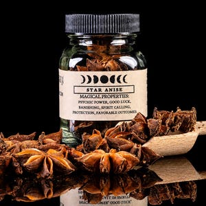 May include: A clear glass jar with a black lid containing dried star anise pods. The label features moon phase icons, the text STAR ANISE, and a list of magical properties including psychic power, good luck, banishing, spirit calling, and protection.