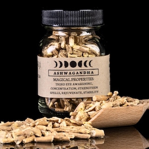 May include: A glass jar filled with dried ashwagandha root pieces. The jar has a black lid and a brown label with the text "Ashwagandha" and "Magical Properties: Third Eye Awakening, Concentration, Strengthen Spells, Rejuvenate, Stability".