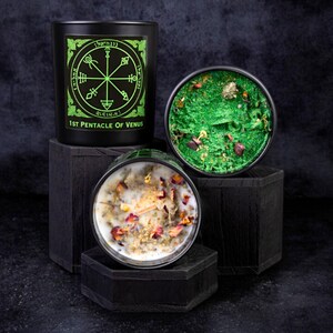 May include: Three black candles with different designs. The first candle has a green and black design with the text "1st Pentacle of Venus". The second candle has a green and gold design. The third candle has a white wax with dried flowers and herbs.