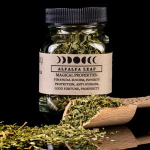 Puede incluir: Un frasco de vidrio lleno de hojas de alfalfa secas. El frasco tiene una tapa negra y una etiqueta marrón que dice "ALFALFA LEAF" y enumera sus propiedades mágicas: "ÉXITO FINANCIERO, PROTECCIÓN CONTRA LA POBREZA, PROTECCIÓN CONTRA EL HAMBRE, BUENA FORTUNA, PROSPERIDAD".