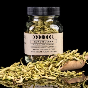 Puede incluir: Un frasco de vidrio con tapa negra, etiquetado "HONEYSUCKLE" y "MAGICAL PROPERTIES". La etiqueta enumera propiedades como buena suerte y pérdida de peso. Flores de madreselva secas alrededor de una cuchara de madera, sobre fondo negro.