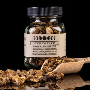 May include: A glass jar filled with dried Devil's Claw herb. The jar has a black lid and a label that reads "Devil's Claw" and lists its magical properties: banishing, purification, attraction, protection, increase desire, and exorcism.