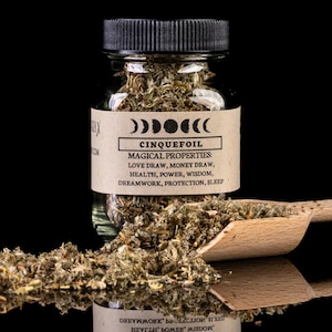 May include: A glass jar with a black lid filled with dried herbs. The label on the jar is brown with black text that reads "Cinquefoil" and lists its magical properties: "Love Draw, Money Draw, Health, Power, Wisdom, Dreamwork, Protection, Sleep".