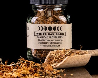 May include: A glass jar filled with dried white oak bark. The jar has a brown label with the text "WHITE OAK BARK" and "MAGICAL PROPERTIES: PROTECTION, GOOD LUCK, FERTILITY, UNCROSSING, STRENGTH, WISDOM". A wooden scoop is filled with the bark and is resting on a black surface.