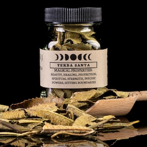 Puede incluir: Un frasco de vidrio lleno de hojas de Yerba Santa secas. El frasco tiene una etiqueta marrón con el texto "Yerba Santa: Propiedades mágicas: Belleza, Sanación, Protección, Fuerza espiritual, Poderes psíquicos, Establecer límites".