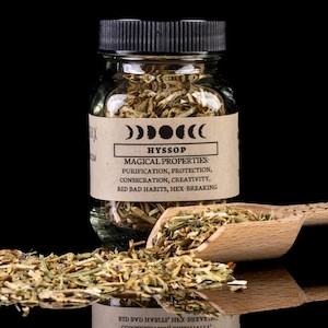 Puede incluir: Un frasco de vidrio de hisopo con tapa negra, una cuchara de madera y hierbas sueltas. La etiqueta dice "HYSSOP" y enumera propiedades mágicas. El fondo es negro, resaltando el producto.