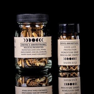 May include: Two glass jars filled with Devil's Shoestring, a root used in hoodoo practices. The jars have black lids and labels with text about protection, good luck, and masculine energy. The background is black.