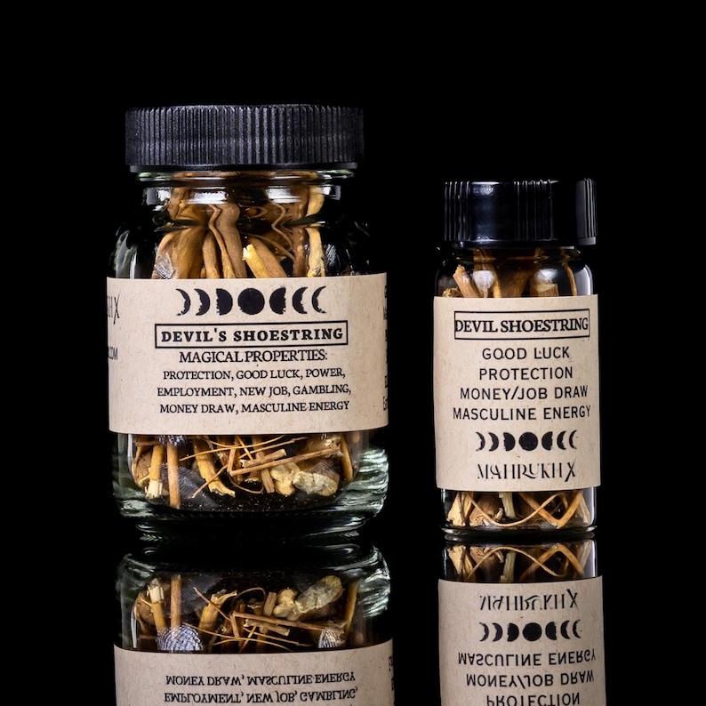 May include: Two glass jars filled with Devil's Shoestring, a root used in hoodoo practices. The jars have black lids and labels with text about protection, good luck, and masculine energy. The background is black.