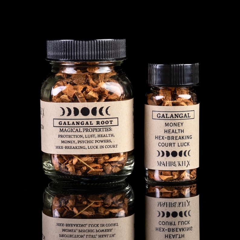 May include: Two glass jars filled with dried herbs, labeled "Galangal Root" and "Galangal". The labels list magical properties and uses for the herbs, including protection, lust, health, money, psychic powers, hex-breaking, and luck in court.