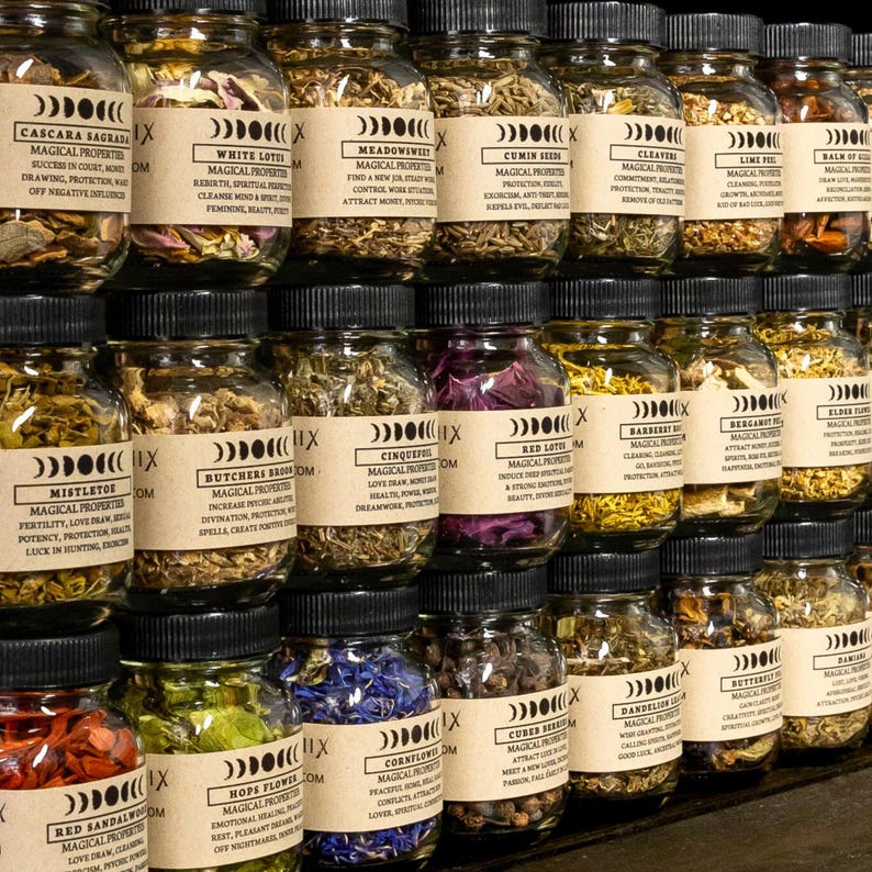 May include: A display of glass jars filled with dried herbs and botanicals, each with a kraft paper label. The jars are stacked in rows, displaying a range of colours and textures. Labels include text such as "Cascara Sagrada" and "White Lotus".