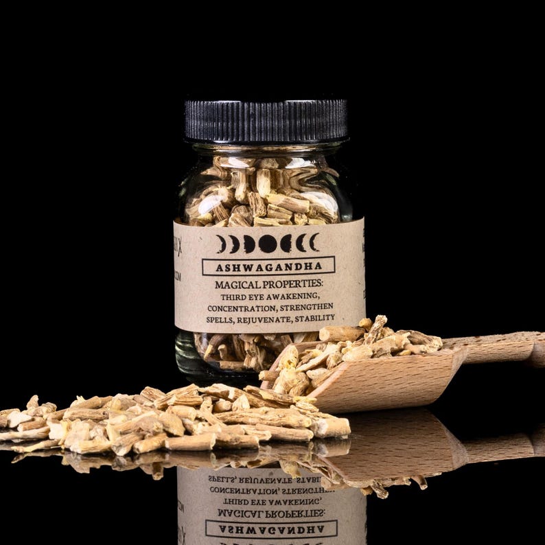 May include: A glass jar filled with dried ashwagandha root pieces. The jar has a black lid and a brown label with the text "Ashwagandha" and "Magical Properties: Third Eye Awakening, Concentration, Strengthen Spells, Rejuvenate, Stability".
