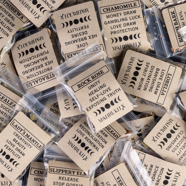 May include: A collection of small plastic bags filled with dried herbs, each with a tan paper label. The labels feature text such as "Rock Rose" and "Chamomile", moon phase symbols, and the brand name "MAHRUKH X".