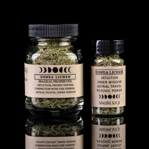 May include: Two glass jars filled with dried green usnea lichen. The jars have brown paper labels with black text that reads "Usnea Lichen" and lists magical properties, including intuition, psychic powers, connection with the unseen, astral travel, and inner wisdom. The labels also feature a crescent moon symbol.