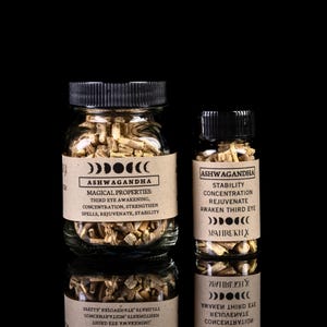 May include: Two glass jars filled with dried herbs, labelled "Ashwagandha". The larger jar has a label with the text "Magical Properties: Third Eye Awakening, Concentration, Strengthen Spells, Rejuvenate, Stability". The smaller jar has a label with the text "Stability Concentration Rejuvenate Awaken Third Eye" and a symbol of three moons.