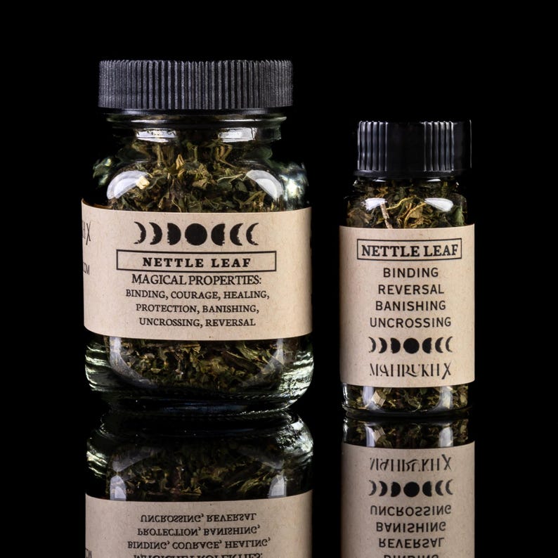 May include: Two glass jars filled with dried nettle leaf. The jars have black lids and labels with the text "Nettle Leaf" and "Magical Properties: Binding, Courage, Healing, Protection, Banishing, Uncrossing, Reversal."