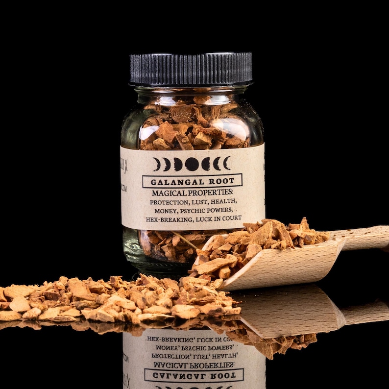 May include: A glass jar filled with dried, light brown galangal root pieces. The jar has a black lid and a brown label with the text 'GALANGAL ROOT' and 'MAGICAL PROPERTIES: PROTECTION, LUST, HEALTH, MONEY, PSYCHIC POWERS, HEX-BREAKING, LUCK IN COURT'.