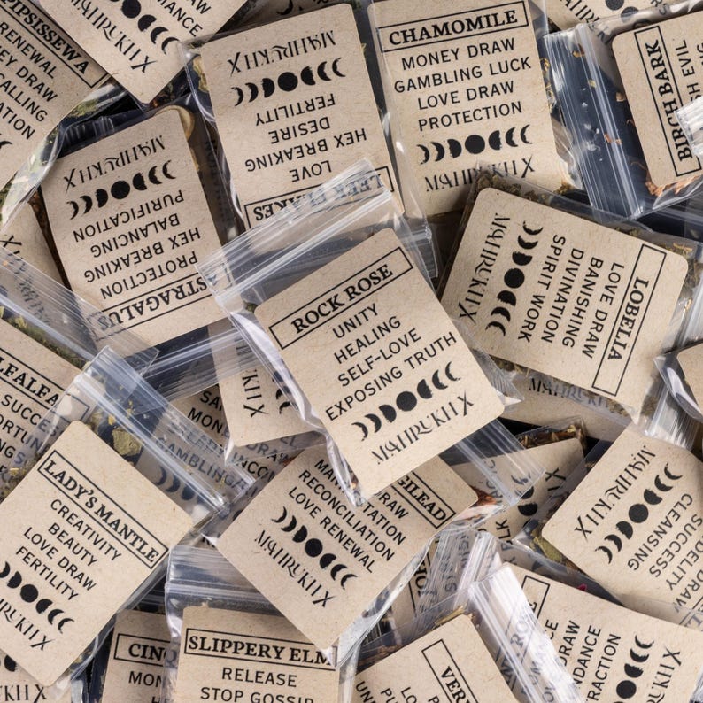 May include: An assortment of small, clear plastic bags filled with dried herbs. Each bag has a tan paper label with black text, including the words "Rock Rose," "Chamomile," and "Lady's Mantle." The labels also feature moon phase graphics.