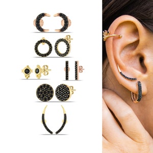 Könnte beinhalten: Ein Set schwarzer und goldener Ohrringe mit verschiedenen Stilen, darunter Creolen, Ohrstecker und Halbmonde. Die Ohrringe sind mit schwarzen Zirkonia-Steinen verziert.