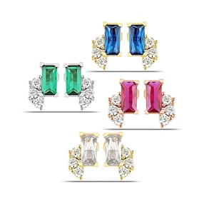 May include: A selection of stud earrings in blue, green, pink, and clear. Each pair has a rectangular gemstone and a cluster of smaller, round gemstones. The earrings are set in gold or silver-toned metal.