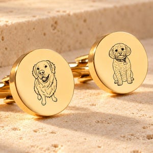May include: A pair of round gold-toned metal cufflinks. Each cufflink features a circular face with a black line-art engraving of a dog. One cufflink displays a golden retriever, while the other shows a small curly-haired dog wearing a collar.