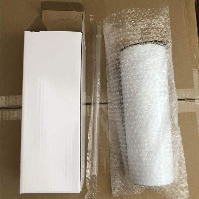 May include: A white tumbler with a black lid is packaged in a white box with a clear plastic straw. The tumbler is wrapped in bubble wrap for protection during shipping.