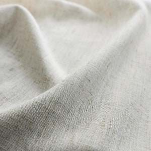 May include: Close-up of a white linen fabric with a textured weave. The fabric is folded and draped, creating soft folds and wrinkles.