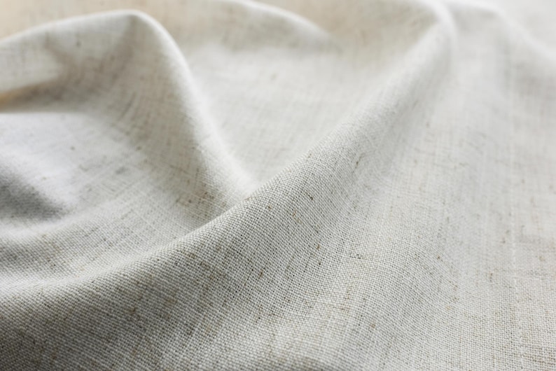 May include: Close-up of a white linen fabric with a textured weave. The fabric is folded and draped, creating soft folds and wrinkles.