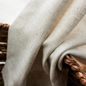 May include: A close-up of a white linen fabric draped over a woven basket. The fabric has a subtle texture and a natural, rustic look.