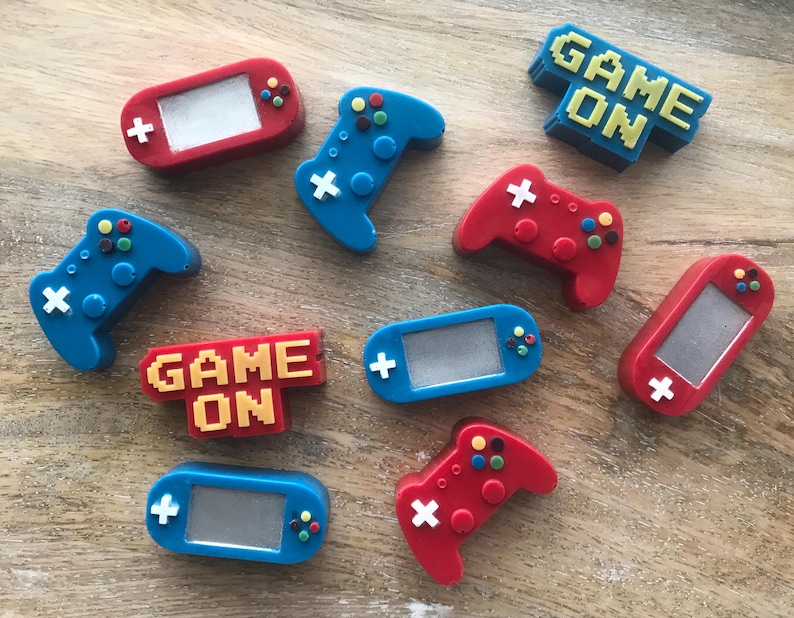 May include: A collection of colorful gaming-themed accessories. The image features red and blue game controllers, handheld consoles, and the phrase "GAME ON" in pixelated lettering. The accessories have white, yellow, and green accents.