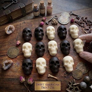 May include: A collection of small, molded skull-shaped treats in alternating black and white colors arranged in a grid. The display includes antique-style props like metal keys, coins, small glass vials, dried rosebuds, and a book, with a plaque reading Sweet American Treat Co.
