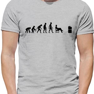 May include: A grey t-shirt featuring a black graphic of the evolution of man, culminating in a man sitting in a chair in front of a television.