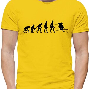 Könnte beinhalten: Ein gelbes T-Shirt mit einer schwarzen Silhouette der Evolution des Menschen, die mit einem Skifahrer endet. Der Skifahrer trägt einen Skihelm und hält Skistöcke.