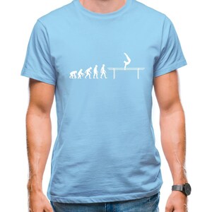 Op de afbeelding: Een lichtblauw t-shirt met een witte afbeelding van een stokfiguur dat een handstand maakt op parallelle bars. De afbeelding toont de evolutie van de mens, beginnend met een aap en eindigend met het stokfiguur op de bars.
