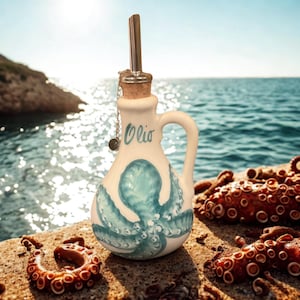 Puede incluir: Una aceitera de cer&aacute;mica blanca con una ilustraci&oacute;n de pulpo azul y la palabra Olio en cursiva. La botella tiene un asa, un tap&oacute;n de corcho y un vertedor de acero inoxidable con una peque&ntilde;a cadena de metal y un dije circular adjunto.
