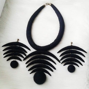 May include: A black felt necklace and earrings set with a crescent moon design. The necklace is a thick band of felt and the earrings are made of multiple crescent moons layered on top of each other.