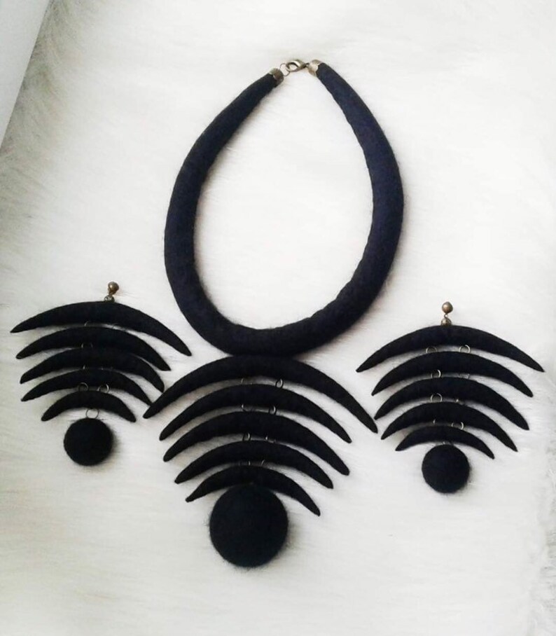 May include: A black felt necklace and earrings set with a crescent moon design. The necklace is a thick band of felt and the earrings are made of multiple crescent moons layered on top of each other.