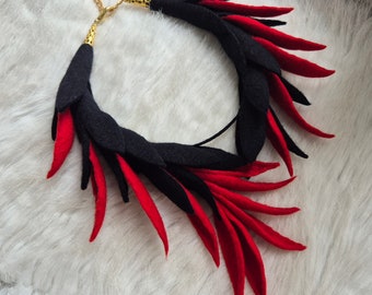 Könnte beinhalten: Eine schwarze und rote Filzkette mit einem goldenen Verschluss. Die Kette besteht aus vielen kleinen Filzstücken, die wie Federn geformt sind. Die Kette ist ein Statement-Stück und wäre perfekt für einen besonderen Anlass.