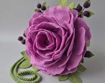 May include: A large, handcrafted felt flower in shades of purple, resembling a rose. The flower is accented with green leaves, small purple berries, and a green rope-like stem. The felt petals are layered, creating a realistic look.
