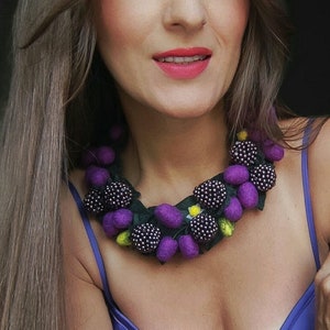 May include: A purple and black felt necklace with berry-shaped beads. The necklace is layered and features green felt leaves.