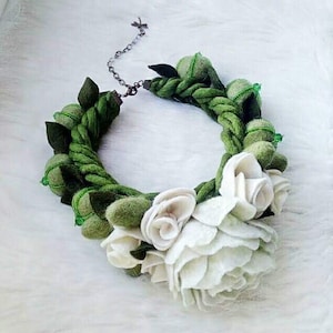 May include: A green felt necklace with white felt flowers. The necklace is made of a braided rope with green felt leaves and beads.