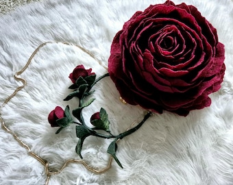 以下が含まれることがあります： ゴールドチェーンストラップが付いた、ワインレッドのフェルト製バラの花のクラッチバッグ。バッグは、緑の葉とワインレッドのフェルト製バラが付いた、フェルト製のバラの茎で飾られています。