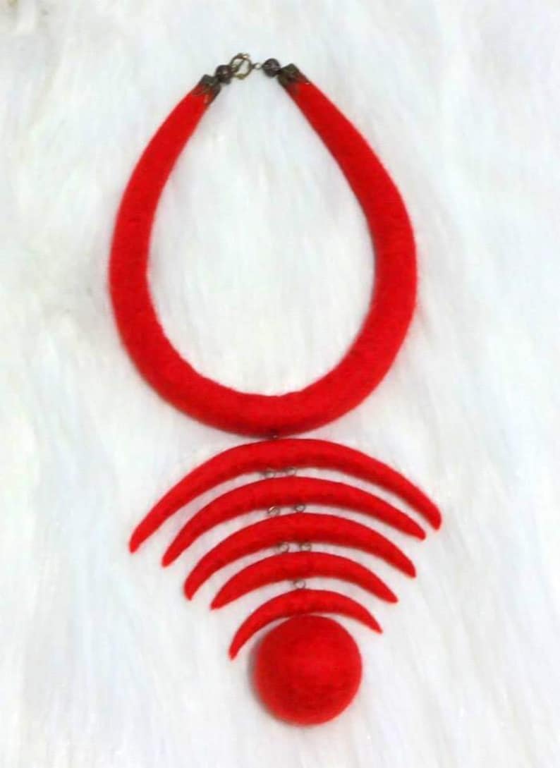 May include: A red felt necklace with a large circle pendant and a series of smaller crescent moon shapes hanging from it.