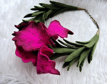 Puede incluir: Un collar de flores de fieltro rosa con hojas de fieltro verde. El collar está hecho de fieltro y tiene una cadena dorada.