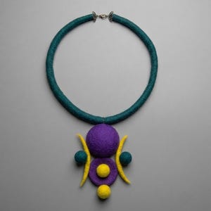 May include: A felted necklace featuring a thick teal circular band with a silver-toned clasp. The pendant consists of a large purple sphere, a smaller purple disc with a yellow center, two teal side spheres, two yellow crescent shapes, and a yellow sphere at the base.