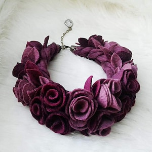 May include: A burgundy felt flower necklace with a small clock charm. The necklace is made of felt roses and leaves.