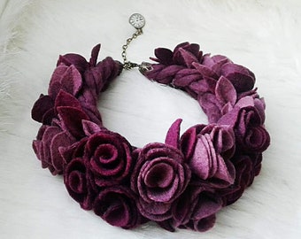 May include: A burgundy felt flower necklace with a small clock charm. The necklace is made of felt roses and leaves.