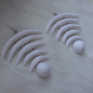 May include: A pair of white felt earrings with a crescent moon shape and a round ball at the bottom.